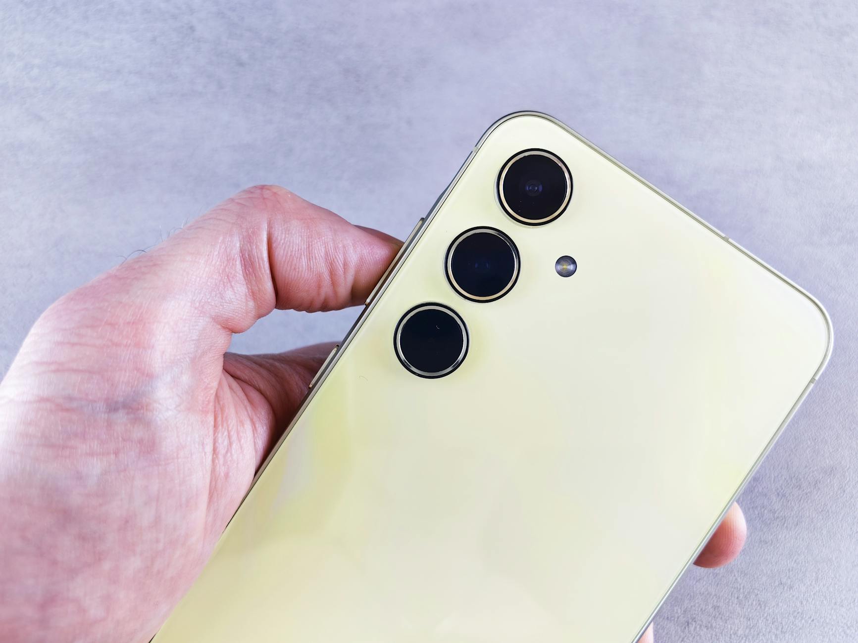 Detailed view of a yellow smartphone highlighting its triple camera lenses held by a hand indoors.